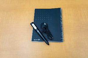 large black digital pen with charging cable and notebook sitting on desk